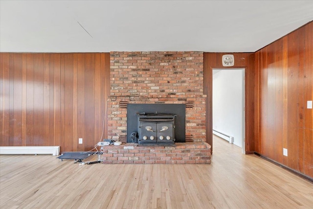 unfurnished living room with a wood stove, wood walls, light hardwood / wood-style floors, and a baseboard radiator