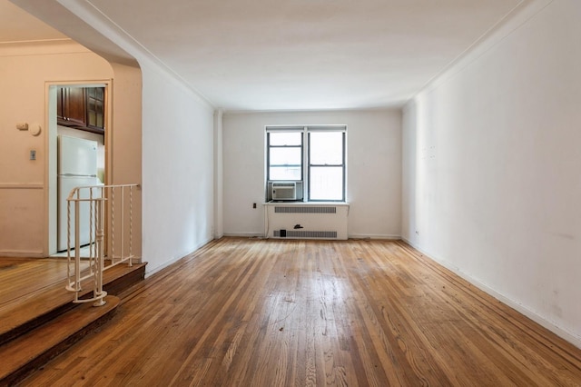 empty room featuring hardwood / wood-style flooring, cooling unit, radiator heating unit, and ornamental molding