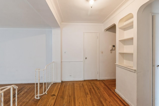 corridor featuring crown molding, built in features, and wood-type flooring