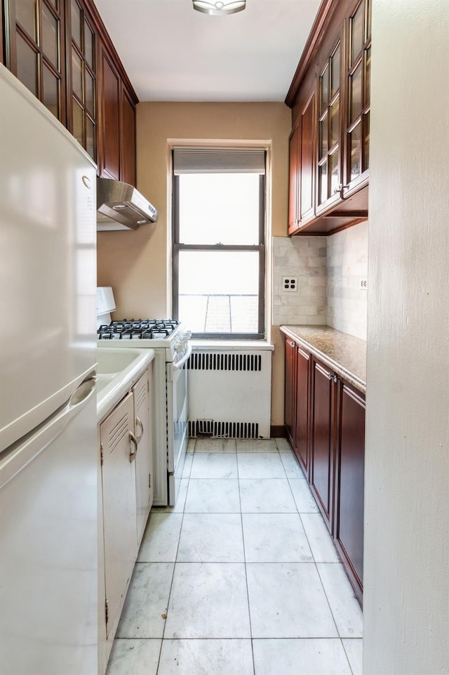 kitchen featuring stainless steel fridge, tasteful backsplash, light tile patterned flooring, radiator heating unit, and white range with gas cooktop