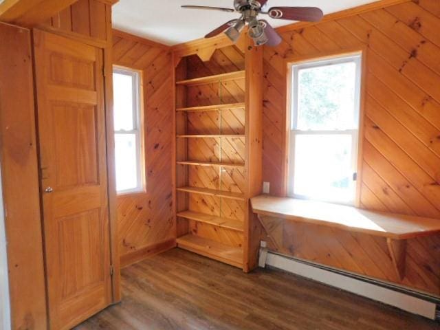 interior space with a baseboard radiator, dark hardwood / wood-style floors, wooden walls, and ceiling fan