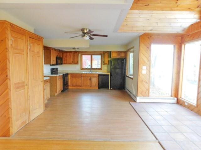 kitchen with wood walls, ceiling fan, black appliances, and light wood-type flooring