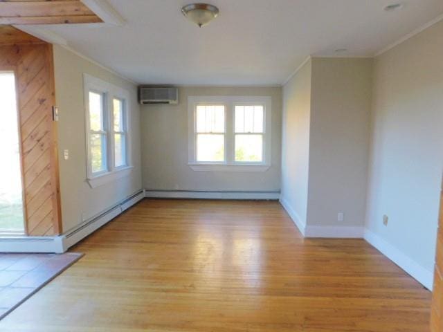 empty room featuring light wood-type flooring, a baseboard radiator, an AC wall unit, and a healthy amount of sunlight