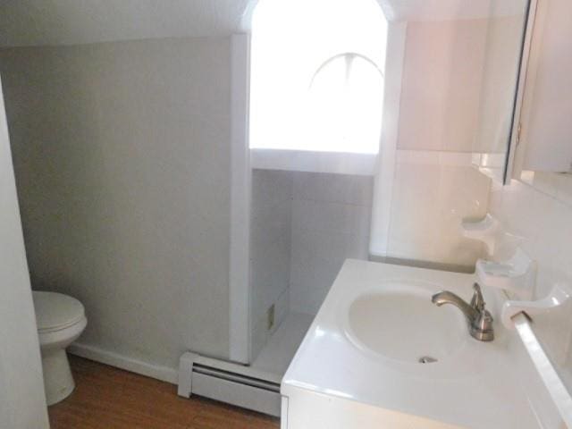 bathroom featuring toilet, vanity, wood-type flooring, and a baseboard heating unit