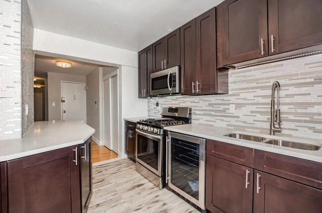 kitchen with sink, beverage cooler, tasteful backsplash, light hardwood / wood-style floors, and appliances with stainless steel finishes