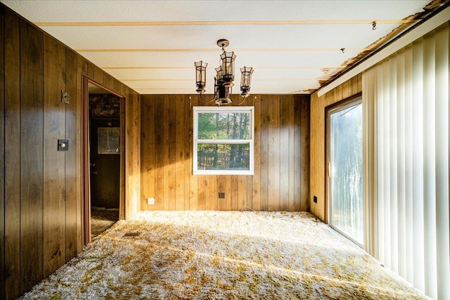 unfurnished dining area featuring wooden walls, carpet floors, and a chandelier