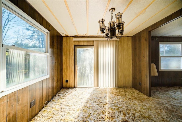 unfurnished room with carpet flooring, a notable chandelier, and wood walls