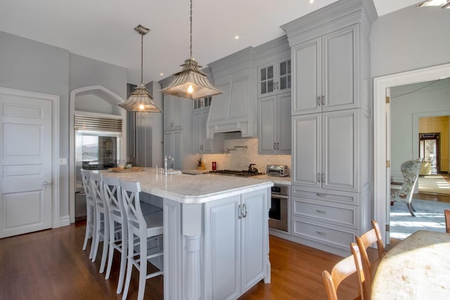 kitchen featuring appliances with stainless steel finishes, tasteful backsplash, an island with sink, hanging light fixtures, and dark hardwood / wood-style floors