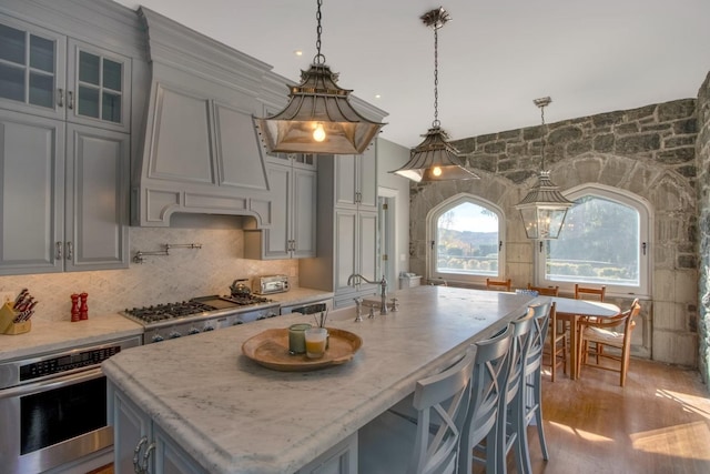 kitchen with hanging light fixtures, light stone counters, a center island with sink, decorative backsplash, and stainless steel appliances