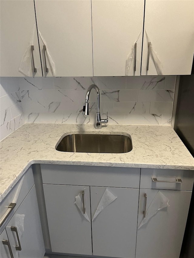 kitchen featuring light stone counters, decorative backsplash, and a sink