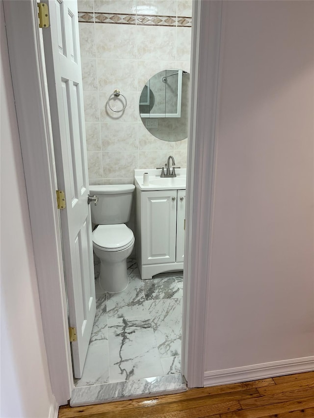 half bathroom with tile walls, marble finish floor, vanity, and toilet