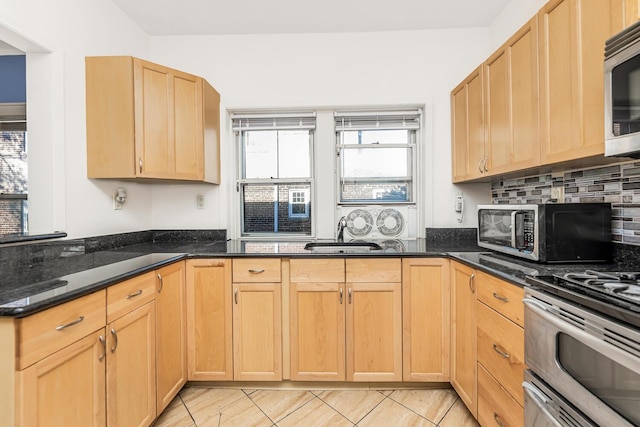 kitchen with sink, stainless steel appliances, dark stone countertops, light brown cabinetry, and light tile patterned floors