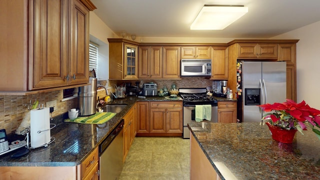 kitchen with dark stone counters, sink, light tile patterned floors, tasteful backsplash, and stainless steel appliances