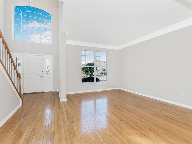 foyer entrance with light hardwood / wood-style floors, crown molding, and a high ceiling