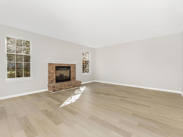 unfurnished living room featuring light hardwood / wood-style floors and a brick fireplace