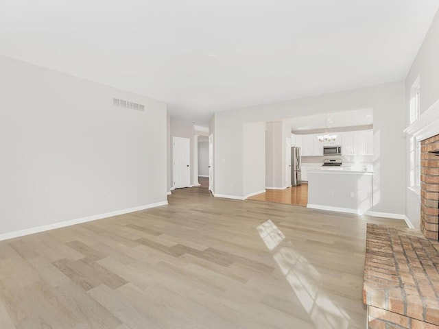 unfurnished living room with a notable chandelier, light wood-type flooring, and a brick fireplace