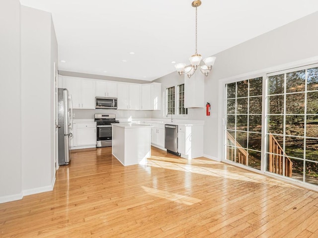 kitchen featuring stainless steel appliances, white cabinetry, hanging light fixtures, and light hardwood / wood-style flooring