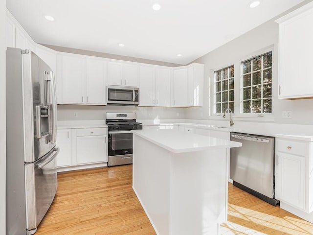 kitchen with white cabinets, a kitchen island, stainless steel appliances, and light hardwood / wood-style floors