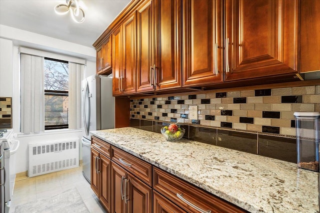 kitchen with light stone countertops, stainless steel fridge, backsplash, radiator, and light tile patterned floors