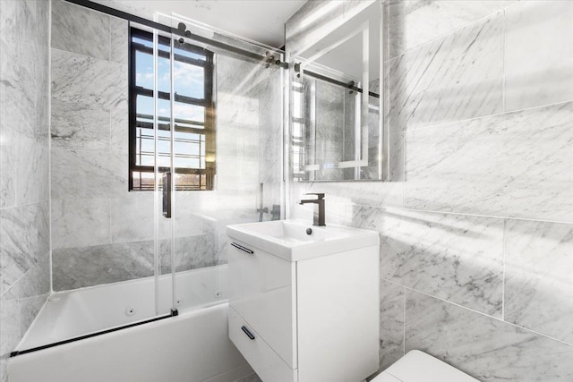 full bathroom featuring vanity, bath / shower combo with glass door, tile walls, and toilet