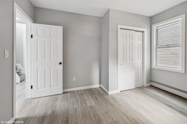 unfurnished bedroom featuring a closet, light hardwood / wood-style floors, and a baseboard heating unit