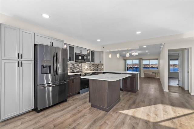 kitchen featuring gray cabinetry, a center island, tasteful backsplash, wood-type flooring, and stainless steel appliances