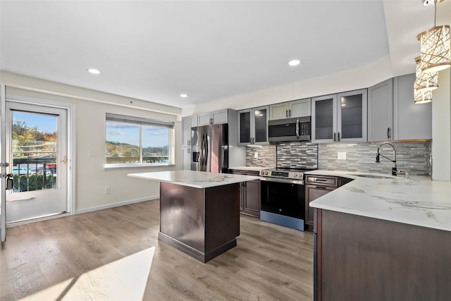 kitchen featuring light stone countertops, appliances with stainless steel finishes, sink, light hardwood / wood-style floors, and hanging light fixtures