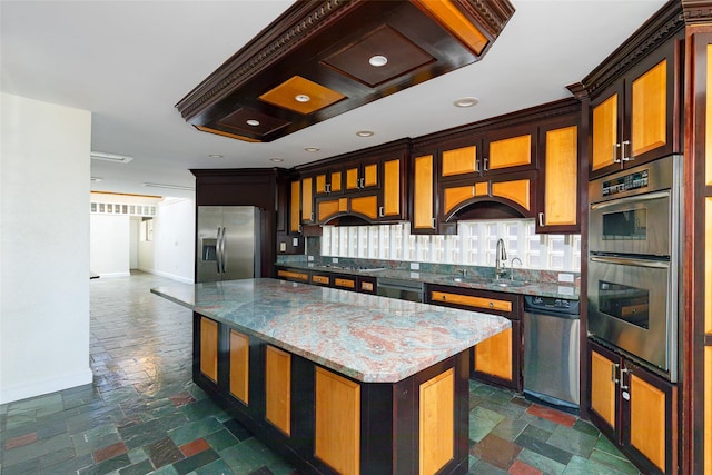 kitchen featuring sink, tasteful backsplash, dark stone counters, a kitchen island, and appliances with stainless steel finishes