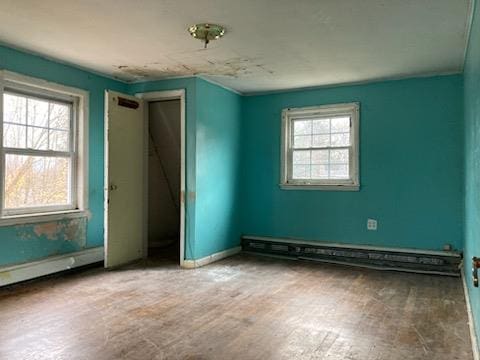 empty room featuring hardwood / wood-style flooring, plenty of natural light, and a baseboard radiator