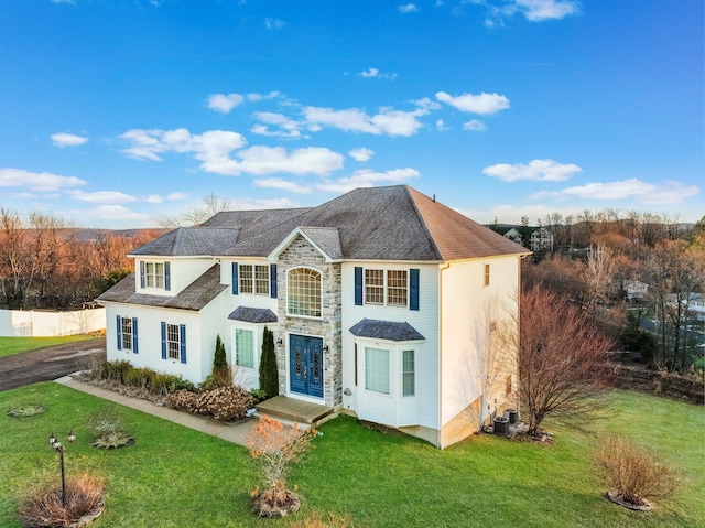 traditional-style house featuring a front yard, stone siding, and central air condition unit