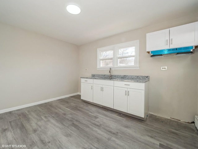 kitchen with white cabinets, light stone countertops, sink, and light hardwood / wood-style flooring