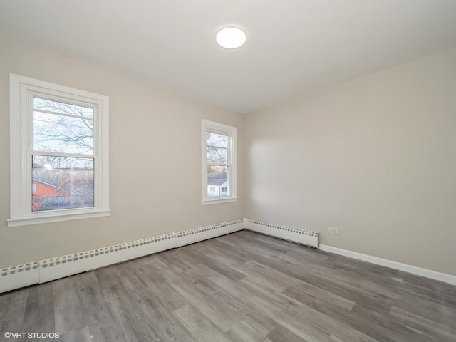 empty room with light hardwood / wood-style flooring, plenty of natural light, and a baseboard heating unit