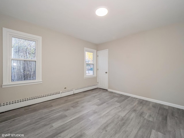 empty room with light hardwood / wood-style flooring, baseboard heating, and a wealth of natural light