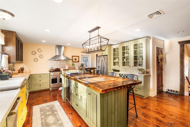 kitchen with a center island, wooden counters, green cabinets, wall chimney exhaust hood, and appliances with stainless steel finishes