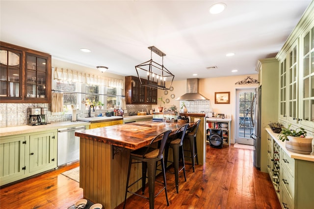 kitchen with green cabinets, wall chimney exhaust hood, appliances with stainless steel finishes, a kitchen island, and dark hardwood / wood-style flooring