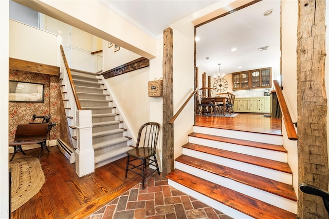 stairway with a notable chandelier, wood-type flooring, a baseboard radiator, and ornamental molding