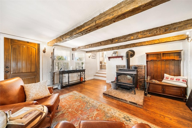 living room featuring beamed ceiling, wood-type flooring, and a wood stove