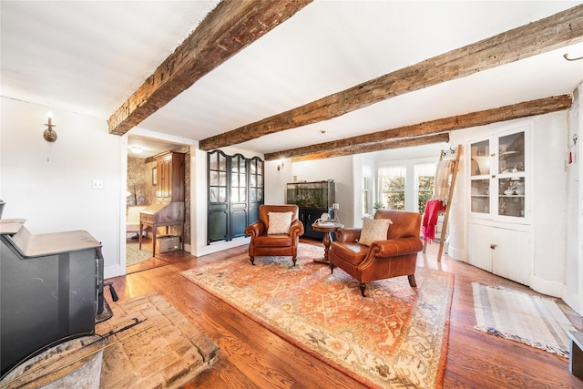 living area with beam ceiling, a wood stove, and light hardwood / wood-style flooring