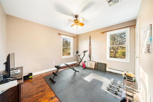 workout room with a baseboard heating unit, dark wood-type flooring, ceiling fan, and a healthy amount of sunlight