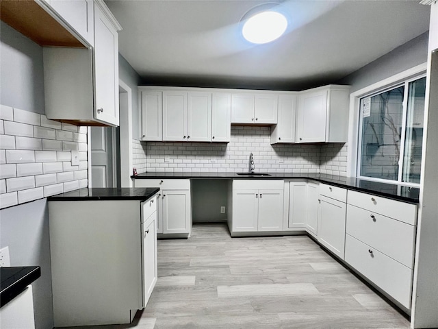 kitchen with backsplash, white cabinetry, light hardwood / wood-style flooring, and sink