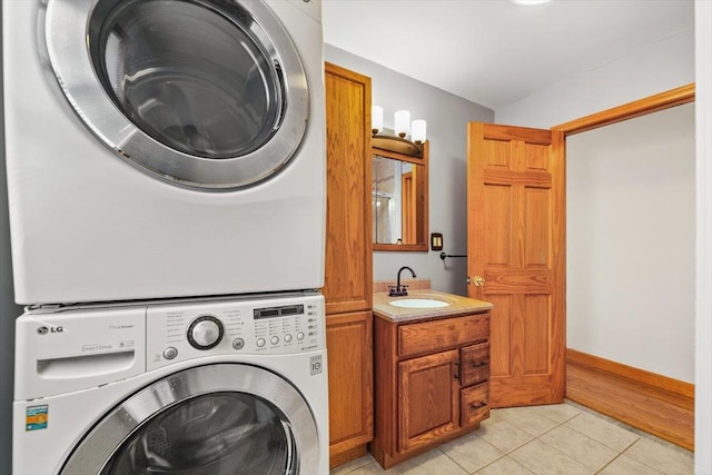 laundry area with cabinets, sink, light tile patterned floors, and stacked washer and dryer