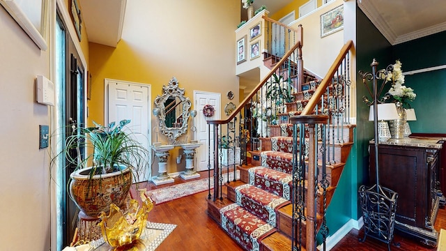 stairway with a towering ceiling, ornamental molding, and wood finished floors