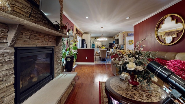 living room featuring wood-type flooring, crown molding, a stone fireplace, and an inviting chandelier