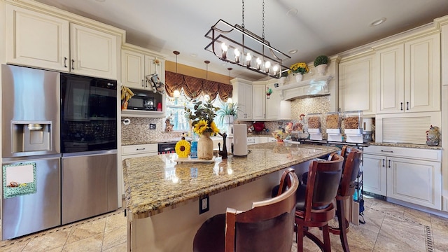 kitchen with light stone countertops, stainless steel fridge, decorative light fixtures, and a center island