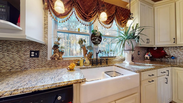 kitchen featuring light stone counters, a sink, cream cabinets, and tasteful backsplash