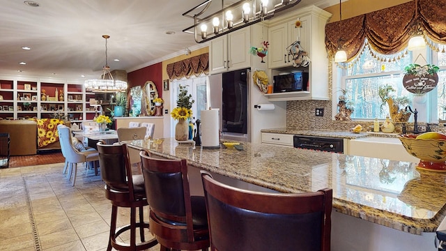 kitchen with light stone counters, a breakfast bar, white cabinetry, black dishwasher, and decorative light fixtures