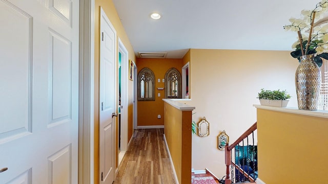 hall with light wood finished floors, attic access, baseboards, an upstairs landing, and recessed lighting