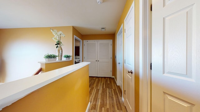 hall featuring light wood-style flooring, visible vents, and an upstairs landing