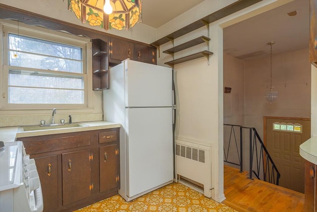 kitchen with radiator, dark brown cabinetry, sink, hanging light fixtures, and white appliances