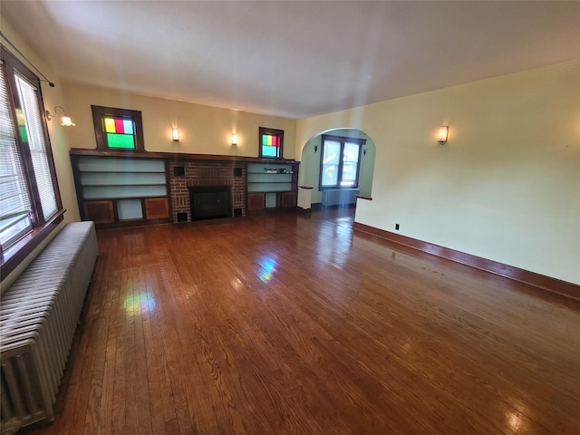 unfurnished living room with dark hardwood / wood-style flooring, radiator heating unit, and a brick fireplace